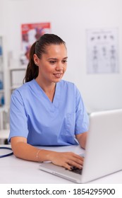 Medical Nurse Typing On Laptop Test Results Of Patient In Hospital Office. Health Care Practitioner Sitting At Desk Using Computer In Modern Clinic Looking At Monitor, Medicine.