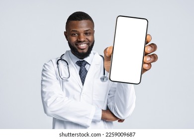 Medical Offer. Black Male Doctor In Uniform Demonstrating Smartphone With Blank Screen At Camera, Smiling African American Physician Man Holding Empty Cellphone In Hand, Collage, Mockup - Powered by Shutterstock