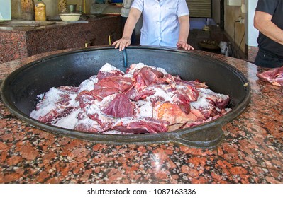 Medical Officer In White Lab Coat Inspecting Meat Covered With Salt & Ready For Cooking In Big Cauldron On Built-in Kitchen Range In Restaurant. Quality Management. Health Control. Selective Focus