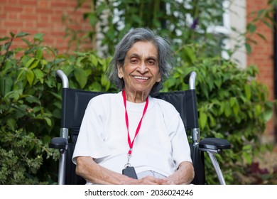 Medical - Old Asian Indian Woman Sitting Smiling In A Wheelchair In A Nursing Home, Care Home Or Garden, UK. Depicts Elderly Healthcare And Retirement