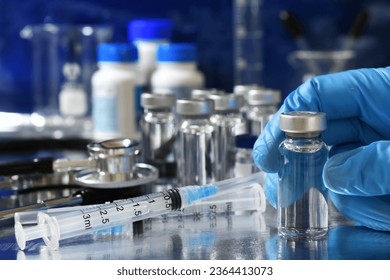 Medical personnel picking up vial of generic vaccine with more immunizations and syringes in background - Powered by Shutterstock