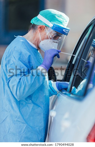 Medical personnel wearing a PPE, performing PCR\
with a swab in their hand, on a patient inside his car to detect if\
he is infected with\
COVID-19