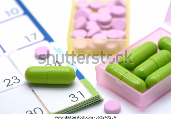Medical pills capsule in pill box with\
calendar on white\
background.
