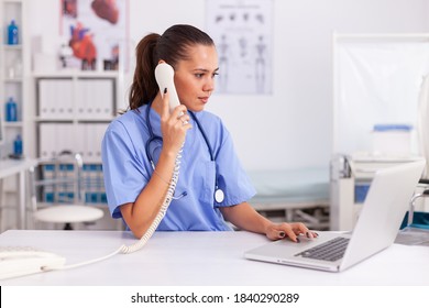 Medical practitioner answering phone calls and scheduling appointments in hospital office. Health care physician sitting at desk using computer in modern clinic looking at monitor. - Powered by Shutterstock
