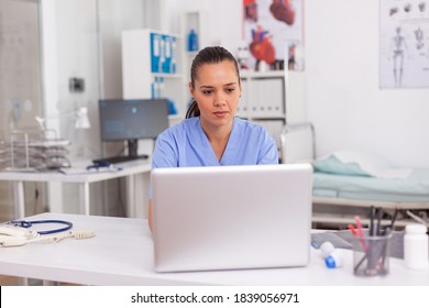 Medical Practitioner Typing Patient Health Report On Laptop In Hospital Office. Health Care Staff Sitting At Desk Using Computer In Modern Clinic Looking At Monitor, Medicine.