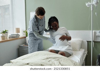 Medical professional assisting pregnant woman in hospital room, providing care and support. Hospital bed and medical equipment creating clinical environment - Powered by Shutterstock