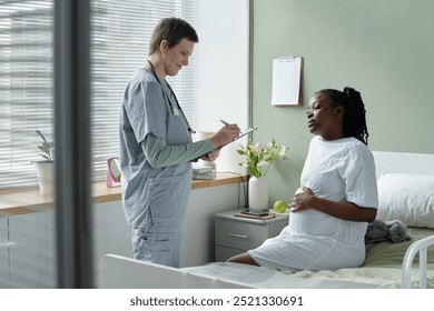 Medical professional conversing with expectant mother in hospital setting while making notes on clipboard, both focused on conversation in a clean and calm environment - Powered by Shutterstock