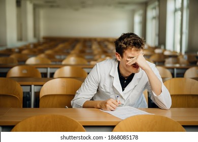 Medical Professional Filling Out A Document, Looking Exhausted, Tired. Doctor Writing An Opinion.Medicine Exam, Medical Practitioner Taking Test Evaluation. Stressed Male Nurse Student In Amphitheater