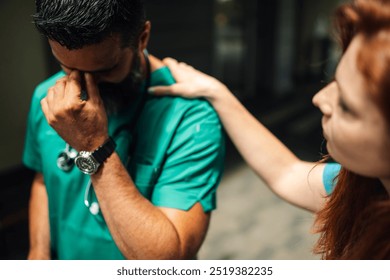 Medical professional in green scrubs, stethoscope around the neck, is distressed and being comforted by a colleague in a hospital corridor. Emotional solidarity among medical staff. - Powered by Shutterstock