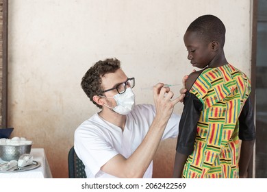 Medical Professional With Protective Face Mask Preparing The Injection Site On The Arm Of A Brave African Schoolboy In Order To To Administer A First Dose Of Antimalarial Vaccine