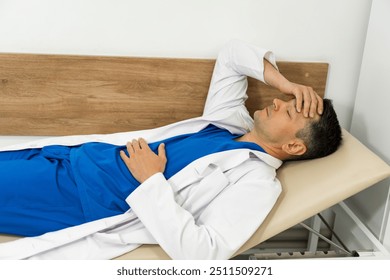 Medical professional resting on an examination table in a clinic room. A healthcare worker lies on a table, wearing scrubs and a lab coat - Powered by Shutterstock