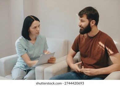Medical professional taking notes while conversing with a male patient in a bright, modern clinic setting during a consultation