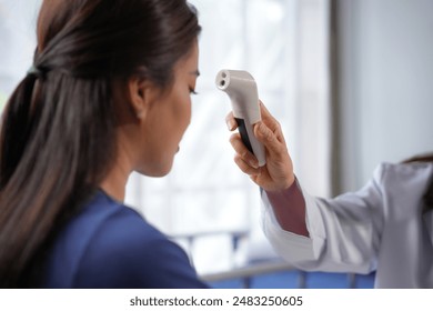 Medical professional is taking a patient's temperature using a contactless digital thermometer, ensuring accurate and hygienic temperature readings - Powered by Shutterstock