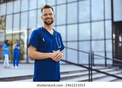 Medical professional working in a hospital. He is dressed in scrubs looking at the camera smiling with a stethoscope around his neck. Happy in his Profession. Male nurse with stethoscope standing  - Powered by Shutterstock