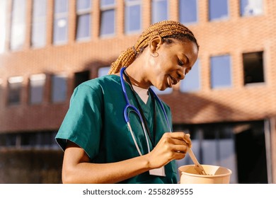 Medical Professionals in casual, candid moments. African American nurse having healthy lunch, snack in front of hospital building, taking break from work. Importance of breaks in healthcare. - Powered by Shutterstock