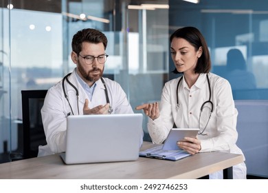 Medical professionals in discussion about patient information using laptop and tablet in modern office setting. Team of healthcare workers collaborating, consulting, and reviewing medical data. - Powered by Shutterstock