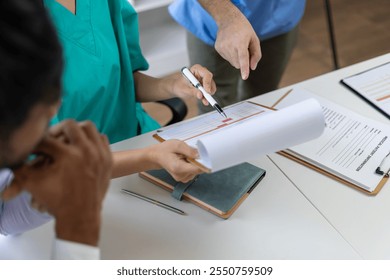 Medical professionals in scrubs discussing patient care, analyzing data on a clipboard in a meeting, Diagnosis and treatment planning. - Powered by Shutterstock