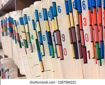 Medical Records Of Patients In Numbered And Color Coded Folders Are Organized And Arranged Numerically And Sequentially In Open Shelves Of A Clinic.