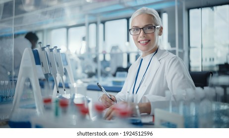 Medical Research Laboratory: Portrait Of A Beautiful Female Scientist Writing Down Data, Smiling On Camera. Advanced Scientific Lab For Medicine, Biotechnology, Microbiology Development