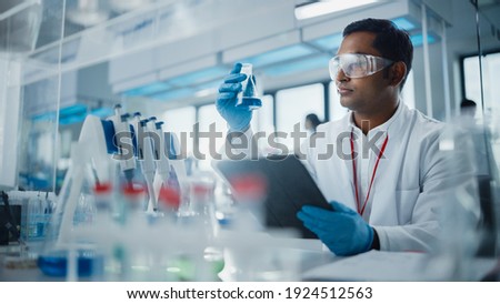 Medical Research Laboratory: Portrait of a Handsome Male Scientist Using Digital Tablet Computer, Analysing Liquid Biochemicals in a Laboratory Flask. Advanced Scientific Biotechnology Laboratory.