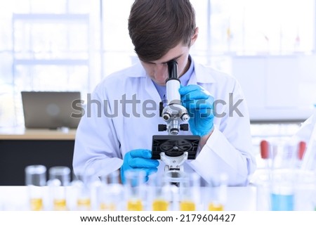 Medical Research Laboratory: Team of professional male scientist working with microscope analysing liquid biochemicals in a laboratory flask. Advanced scientific biotechnology laboratory. 