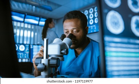 Medical Research Scientist Looking under the Microscope in the Laboratory. Neurologist Solving Puzzles of the Mind and Brain. In the Laboratory with Multiple Screens Showing MRI / CT Brain Scan Images