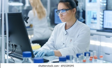 Medical Research Scientist Typing Information Obtained From New Experimental Drug Trial. She Works In A Bright And Modern Laboratory.