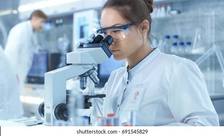 Medical Research Scientists Looking At Samples Under Microscope. She Works In A Bright Modern Laboratory.