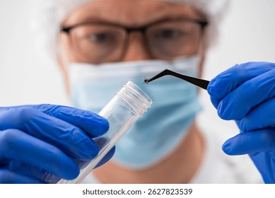 Investigador médico que lleva el equipo protector que transfiere cuidadosamente la muestra de la garrapata en el tubo de ensayo usando las pinzas precisas durante la investigación científica en ambiente estéril del laboratorio