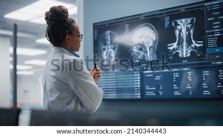 Medical Science Hospital: Confident Black Female Neurologist, Neuroscientist, Neurosurgeon, Looks at TV Screen with MRI Scan with Brain Images, Thinks about Sick Patient Treatment Method. Saving Lives Foto stock © 