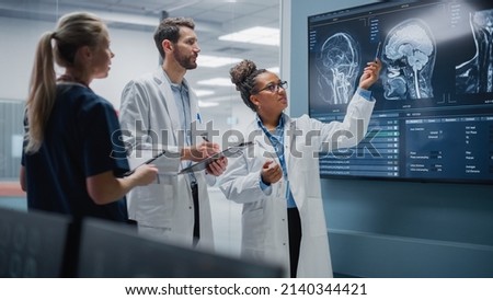 Medical Science Hospital Lab Meeting: Diverse Team of Neurologists, Neuroscientists, Neurosurgeon Consult TV Screen Showing MRI Scan with Brain Images, Talk About Treatment Method, New Drugs Cure