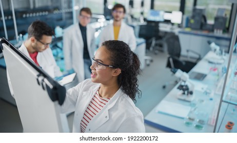 Medical Science Laboratory: Beautiful Black Female Scientist Writes Detailed Project Data Analysis on the Board, Her Diverse Team of Colleague Listens. Young Scientists Solving Problems. - Powered by Shutterstock