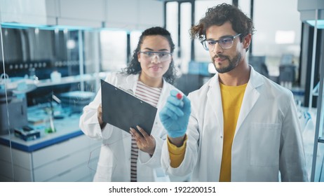 Medical Science Laboratory: Handsome Latin Male Scientist Writes Project Data Analysis on the Glass Board, His Black Female Colleague Checks Information on Clipboard. Young Scientists Solving Problems - Powered by Shutterstock