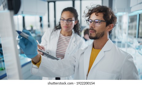 Medical Science Laboratory: Handsome Latin Male Scientist Writes Detailed Project Data Analysis on the Board, His Black Female Colleague Talks. Young Scientists Solving Problems. - Powered by Shutterstock