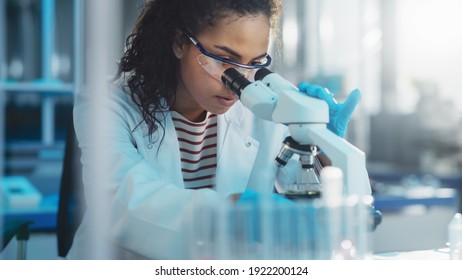 Medizinisches Wissenschaftslabor: Portrait von Schönem Schwarzen Wissenschaftler, die unter Mikroskop schauen, macht Analyse der Testprobe. ambitionierter junger Biotechnologie-Spezialist, der mit fortschrittlicher Ausrüstung arbeitet