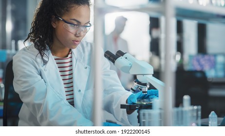 Medizinisches Wissenschaftslabor: Portrait von Beautiful Black Scientist mit Mikroskop, macht Analyse der Testprobe. ambitionierter junger Biotechnologie-Spezialist, der mit fortschrittlicher Ausrüstung arbeitet