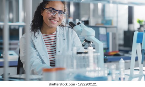 Medical Science Laboratory: Portrait Of Black Scientist Using Microscope For Analysis Of Test Sample, Smileing On Camera. Ambitious Young Biotechnology Specialist, Working With Advanced Equipment