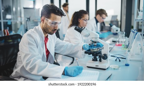 Medical Science Laboratory: Portrait Shot of a Handsome Latin Scientist Looking Under Microscope, Doing Sample Analysis. Young Biotechnology Specialist, Using Advanced Equipment.