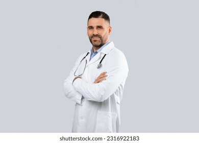 Medical services concept. Portrait of middle aged man doctor therapist in uniform posing with folded arms and looking at camera over light studio background, copy space - Powered by Shutterstock