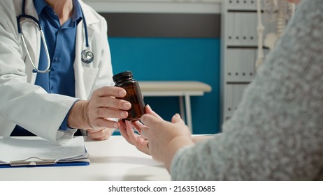 Medical Specialist Giving Disease Treatment On Health Care Prescription, Showing Bottle With Pills And Vitamins To Retired Patient For Recovery. Flask Of Drugs And Painkillers Medication.