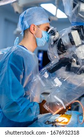 Medical Specialist Performing Surgery Using Modern Equipment. Profile Of Surgeon In Mask Looking Into Microscope In The Operating Room.