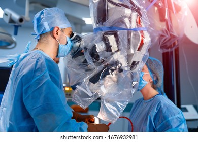 Medical Specialist Performing Surgery Using Modern Equipment. Profile Of Surgeon In Mask Looking Into Microscope In The Operating Room.