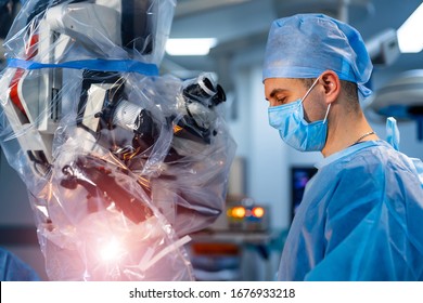 Medical Specialist Performing Surgery Using Modern Equipment. Profile Of Surgeon In Mask Looking Into Microscope In The Operating Room.