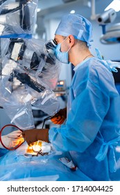 Medical Specialist Performing Surgery Using Modern Equipment. Profile Of Surgeon In Mask Looking Into Microscope In The Operating Room.