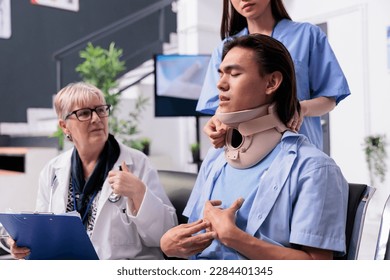 Medical staff helping asian patient with neck brace removing cervical neck collar after injury accident during consultation.. Injured young adult healing fracture and trauma in hospital waiting area - Powered by Shutterstock