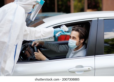 Medical staff make temperature inspection for male in car during covid-19 lockdown. New normal. Paramedic in hazmat suit checks young driver in protective mask in auto through window, free space - Powered by Shutterstock