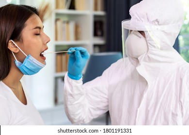 Medical Staff With PPE Suit Test Coronavirus Covid-19 To Asian Woman By Throat Swab At Home. New Normal Health Care Service At Home And Medical Delivery And COVID-19 Testing Concept.