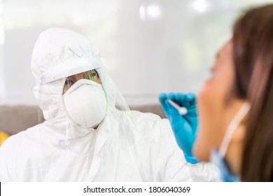 Medical Staff With PPE Suit Test Coronavirus Covid-19 To Asian Woman By Throat Swab At Home. New Normal Health Care Service At Home And Medical Delivery And COVID-19 Testing Concept.