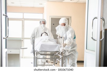 Medical Staff Service Wear Full PPE Caring The Patient By Hospital Bed Trolleys Go To Negative Pressure Room At Emergency Department. Two Hospital Porter Move The Patient By Stretcher. Corona Virus.