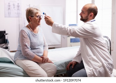 Medical staff using infrared thermometer to take old woman patient body temperature.Medical consultation for infections and disease during global pandemic,flu, tool, sickness.